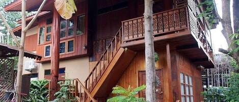 Una casa de madera con balcón, escaleras y una hoja grande colgando del tejado.