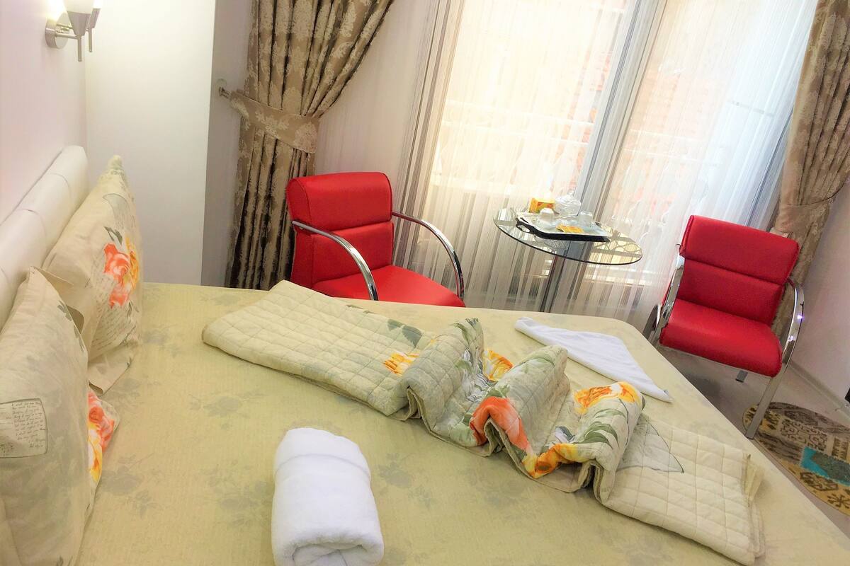Ein Hotelzimmer mit einem Bett, zwei roten Sesseln, einem kleinen Tisch mit Tablett und Vorhängen.