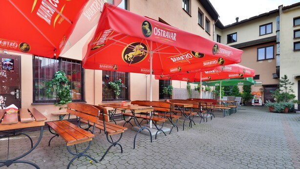 Outdoor seating with red umbrellas, wooden benches, and a paved area. - Hotel Isora (Ostrava)