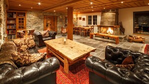 A cozy living room with a stone fireplace, leather sofas, a wooden coffee table, and a stone wall bookshelf. - Griesalp Hotels (Reichenbach im Kandertal)