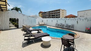 Un área de piscina en la azotea con sillones de descanso, una pequeña mesa y un espacio para sentarse.