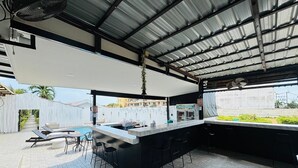Un área de bar moderna al aire libre con piscina, taburetes y vistas del entorno.