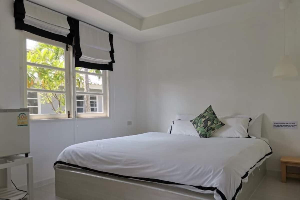 Een slaapkamer met een bed, een raam met gordijnen, een nachtkastje en een wandlamp.
