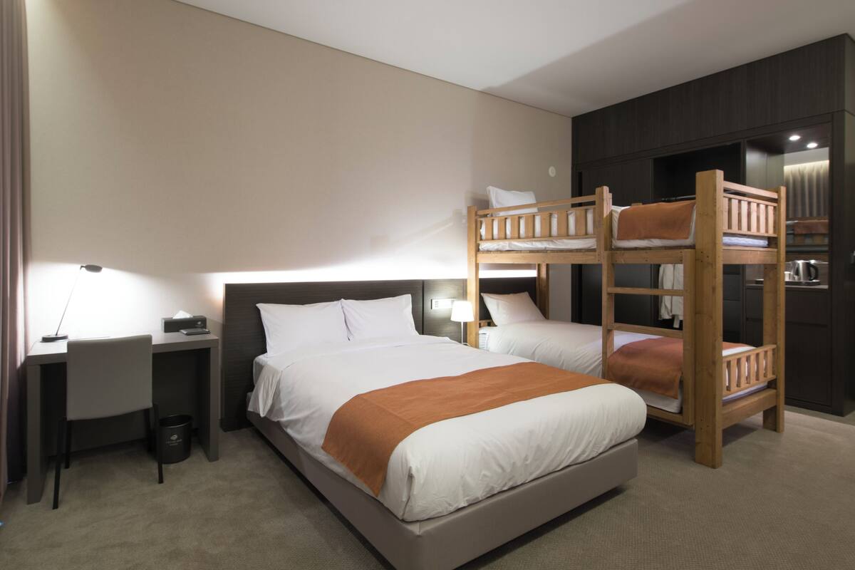 A hotel room with a large bed, a desk, a computer, and a bunk bed.