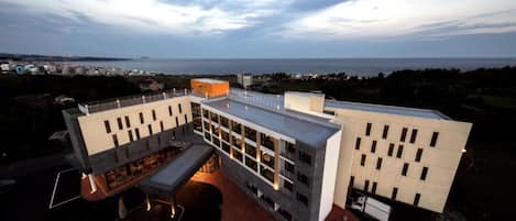 Un edificio moderno con techo plano, amplios ventanales y un área de estacionamiento que incluye un espacio reservado para personas con movilidad reducida.
