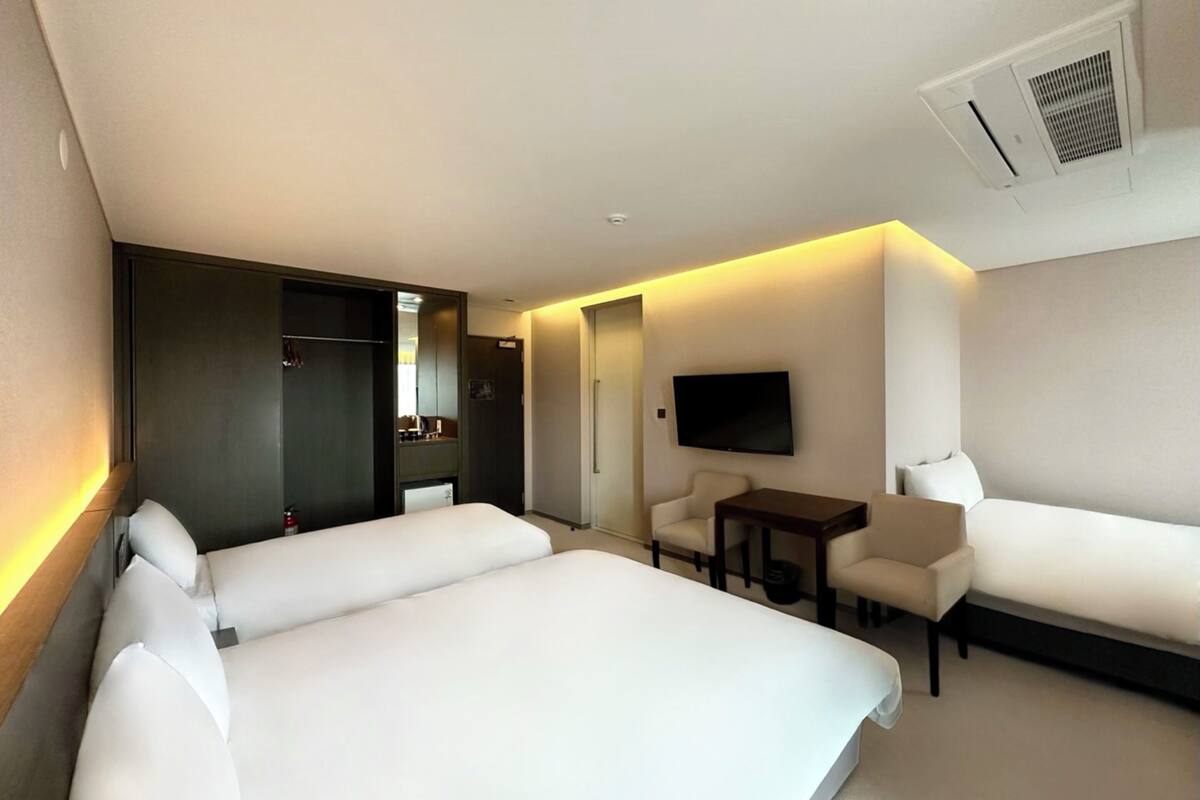 A hotel room with a large bed, a sofa, a small table, a TV, and a mirror.