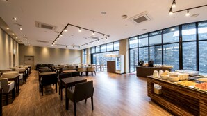A spacious conference room with rows of tables and chairs, a buffet area with food, and large windows offering a city view. - Grand Mer Hotel Jeju (Seogwipo)