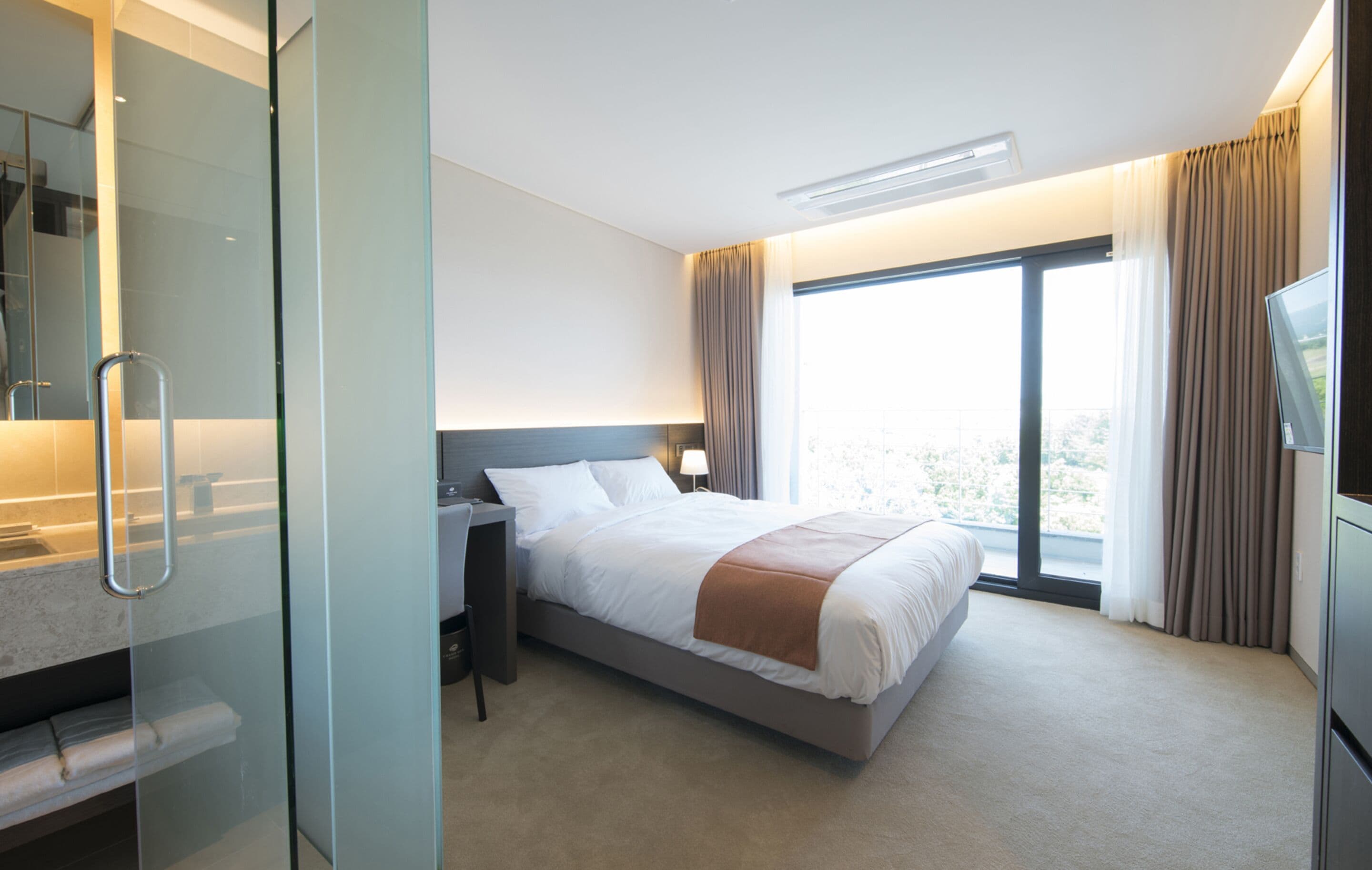 Une chambre d’hôtel moderne dotée d’un grand lit, d’un bureau, d’une télévision et d’une douche à parois de verre.