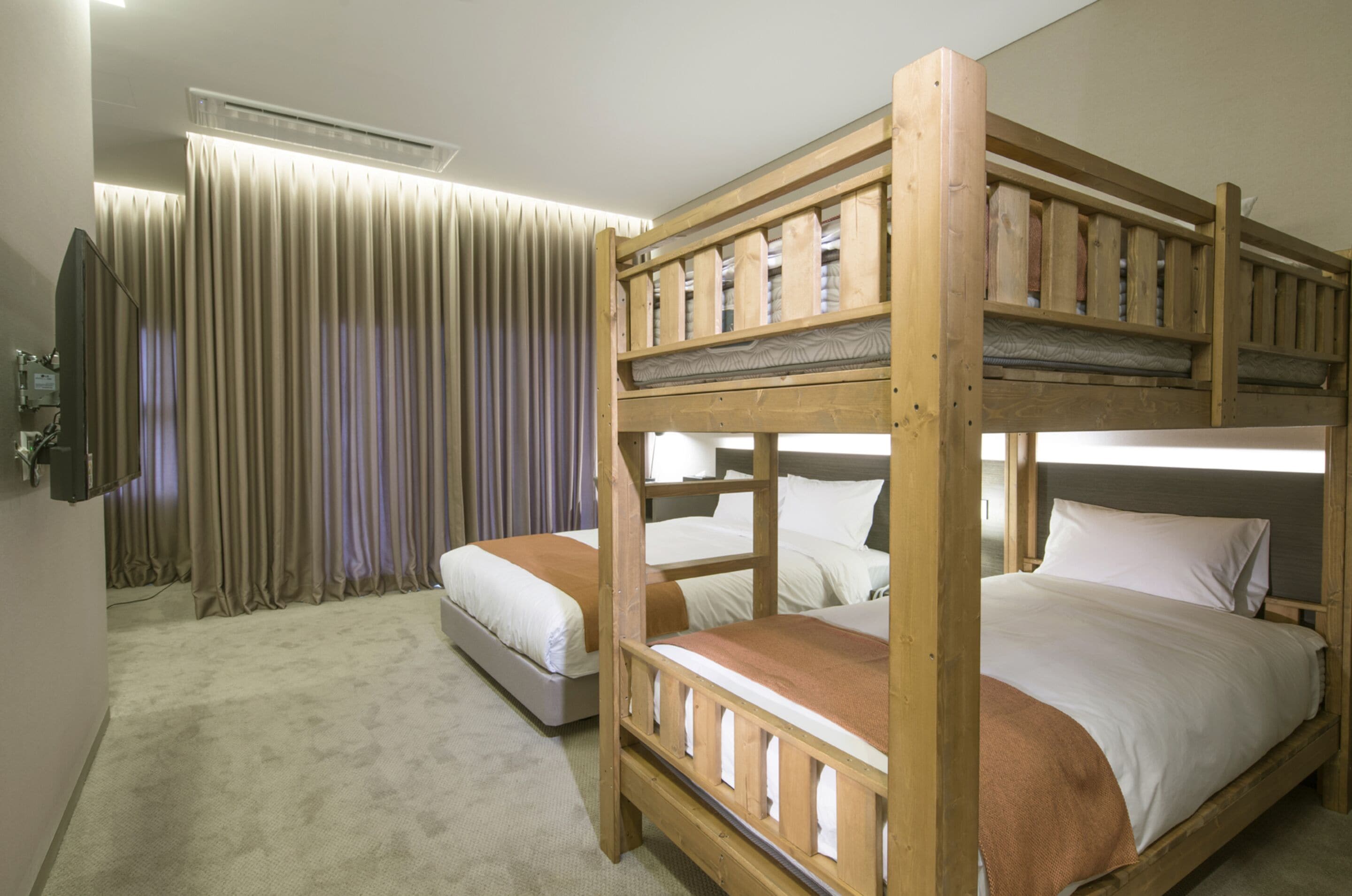 A room with two bunk beds, a flat bed, a television, and a curtain.