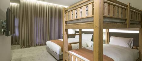 A room with two bunk beds, a flat bed, a television, and a curtain.