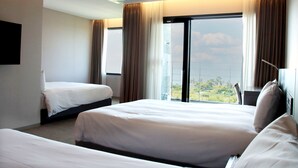 A hotel room with two beds, a large window with curtains, and a view of the outdoors. - Grand Mer Hotel Jeju (Seogwipo)