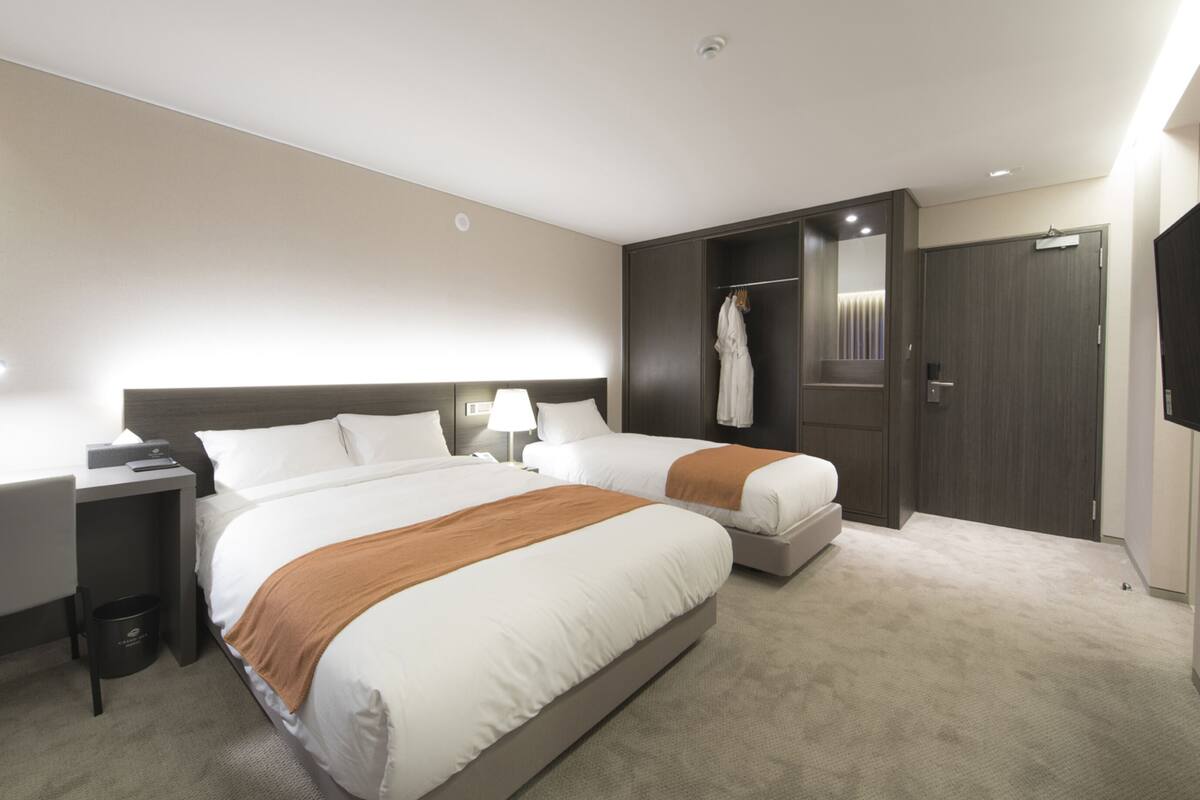 A hotel room with two beds, a desk, a chair, a wardrobe, and a television.