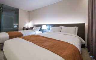 Una habitación de hotel con dos camas, un escritorio, una silla y una lámpara.