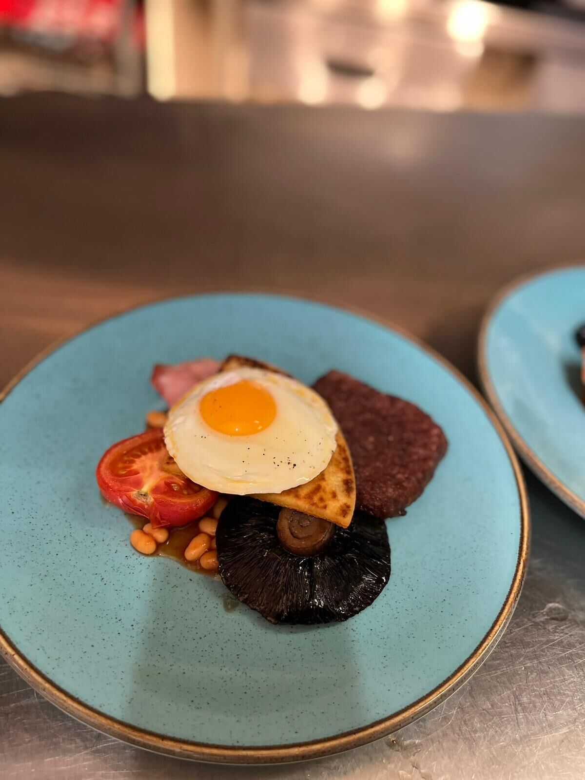 Un plato con un huevo frito, una rodaja de tomate, champiñón y frijoles.
