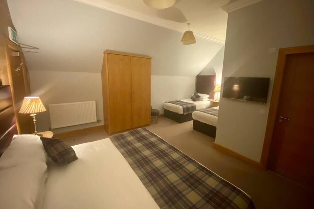 A bedroom with a bed, a wardrobe, a bedside table with a lamp, a television, and a window.