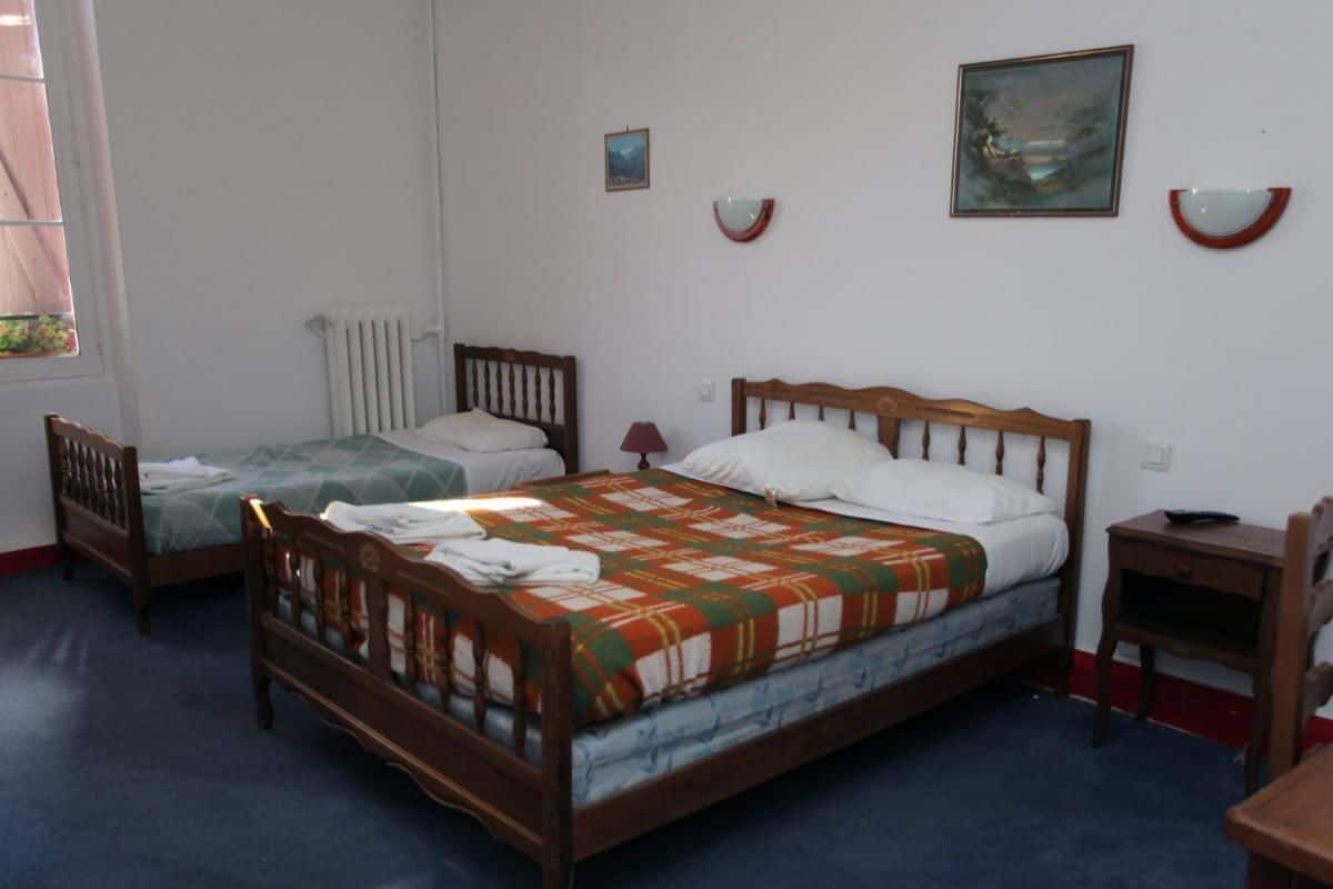 A room with two wooden beds, a small table, and a chair.