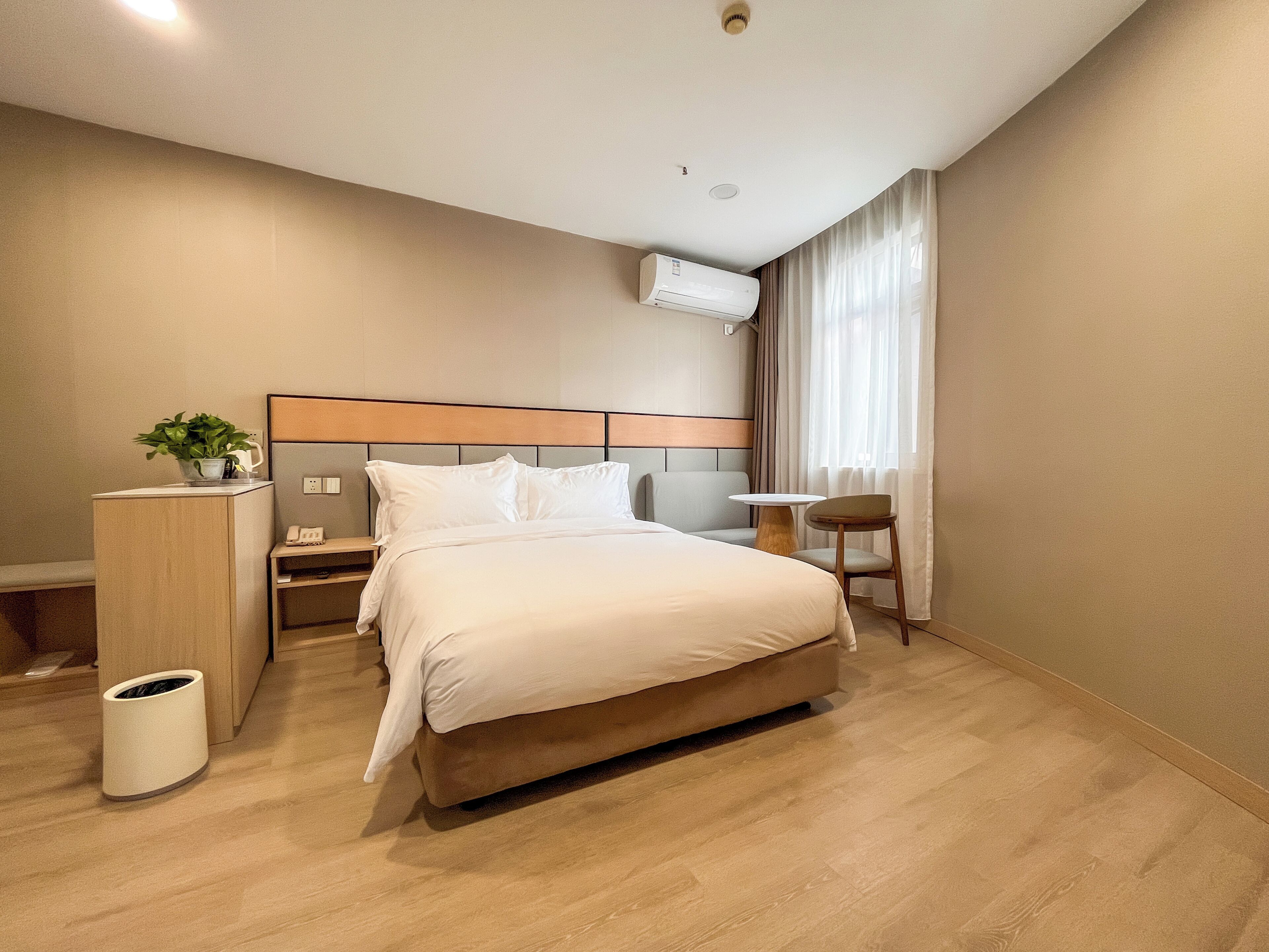 A hotel room with a bed, bedside table, lamp, and a small table with a chair.
