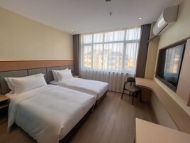A hotel room with two beds, a desk, a chair, a TV, and a window with curtains.