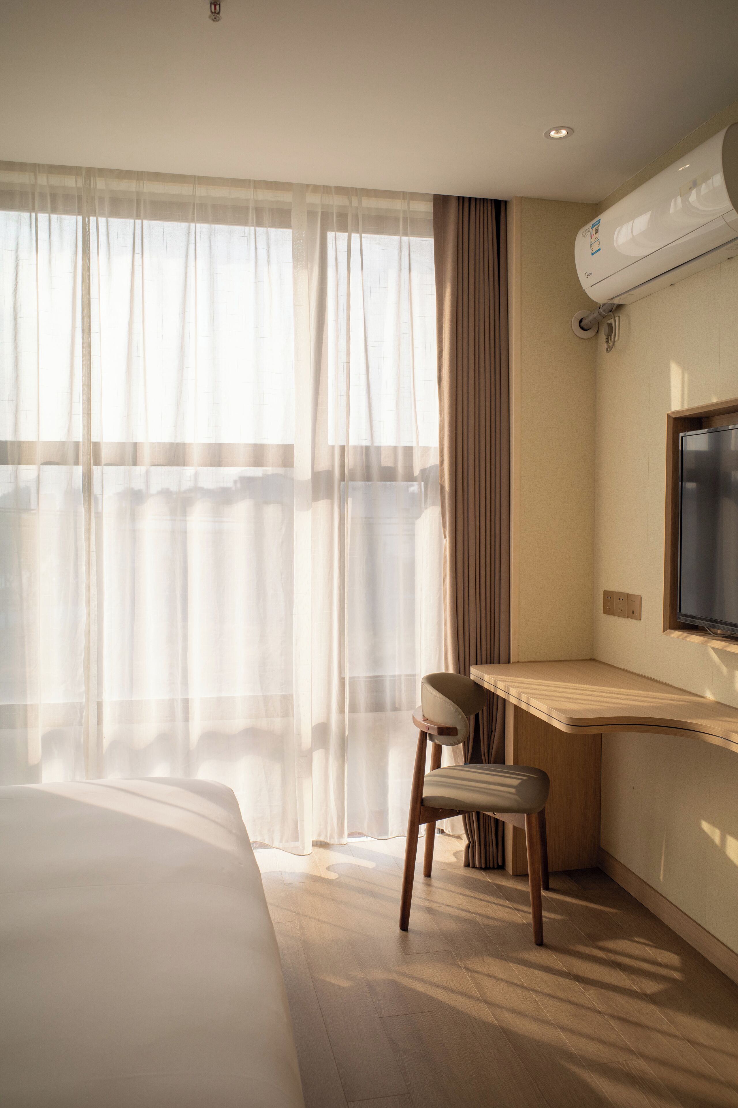 Ein Hotelzimmer mit Bett, Schreibtisch mit Stuhl, Flachbildfernseher und Klimaanlage.