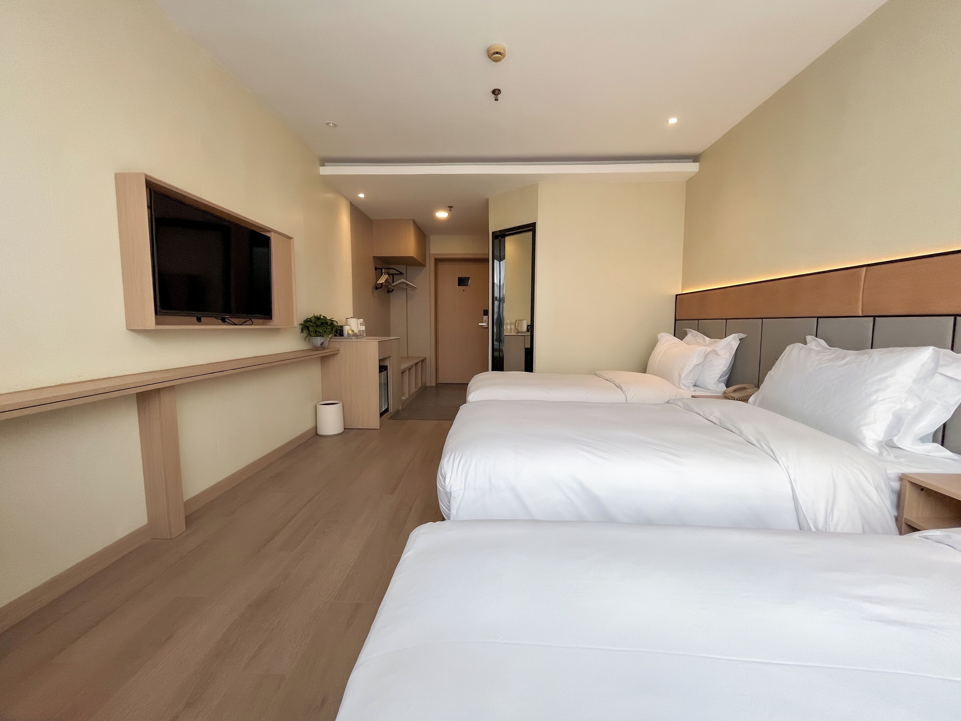 A hotel room with two beds, a TV mounted on the wall, a small kitchenette, and a bathroom visible through an open door.