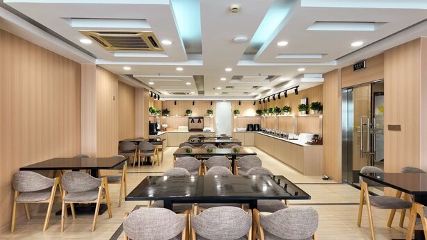 A modern dining area with multiple tables and chairs, a kitchen in the background, and a refrigerator on the right. - Shanghai Joyful Star Hotel (Shanghai)