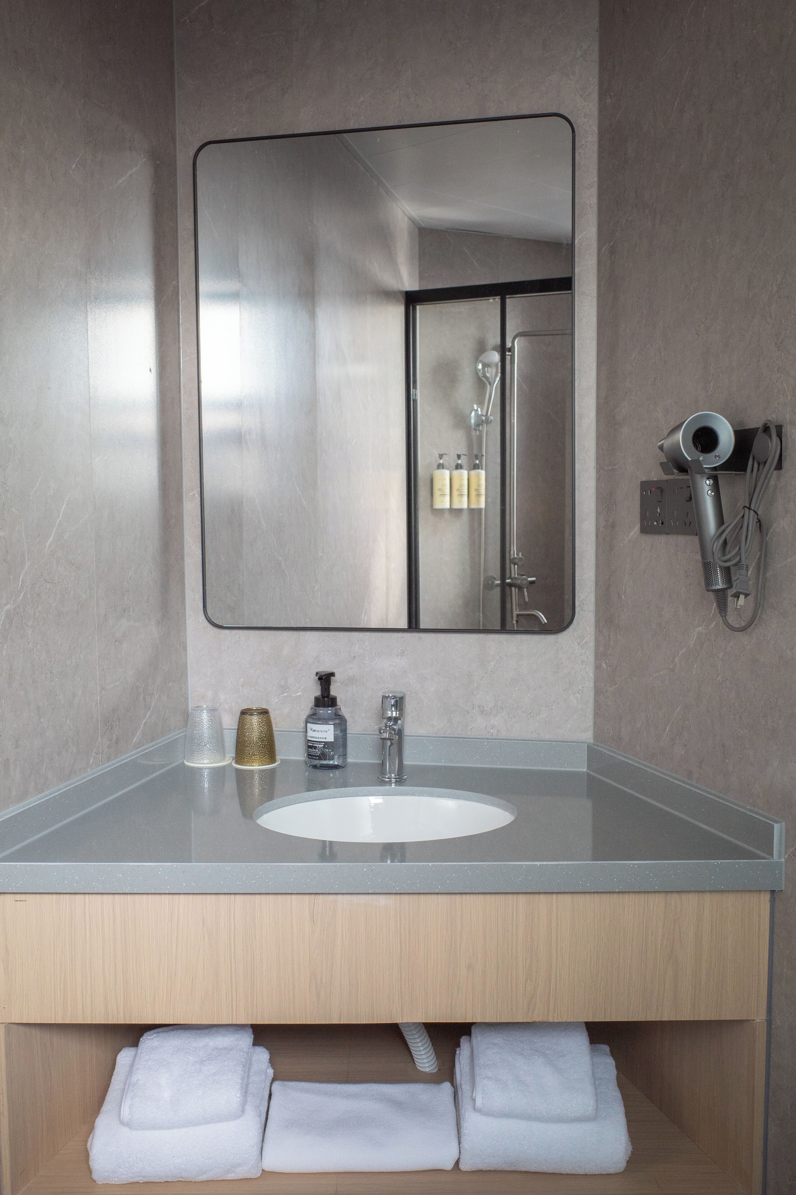 Un baño moderno con un espejo grande, un lavamanos y un secador de pelo montado en la pared.