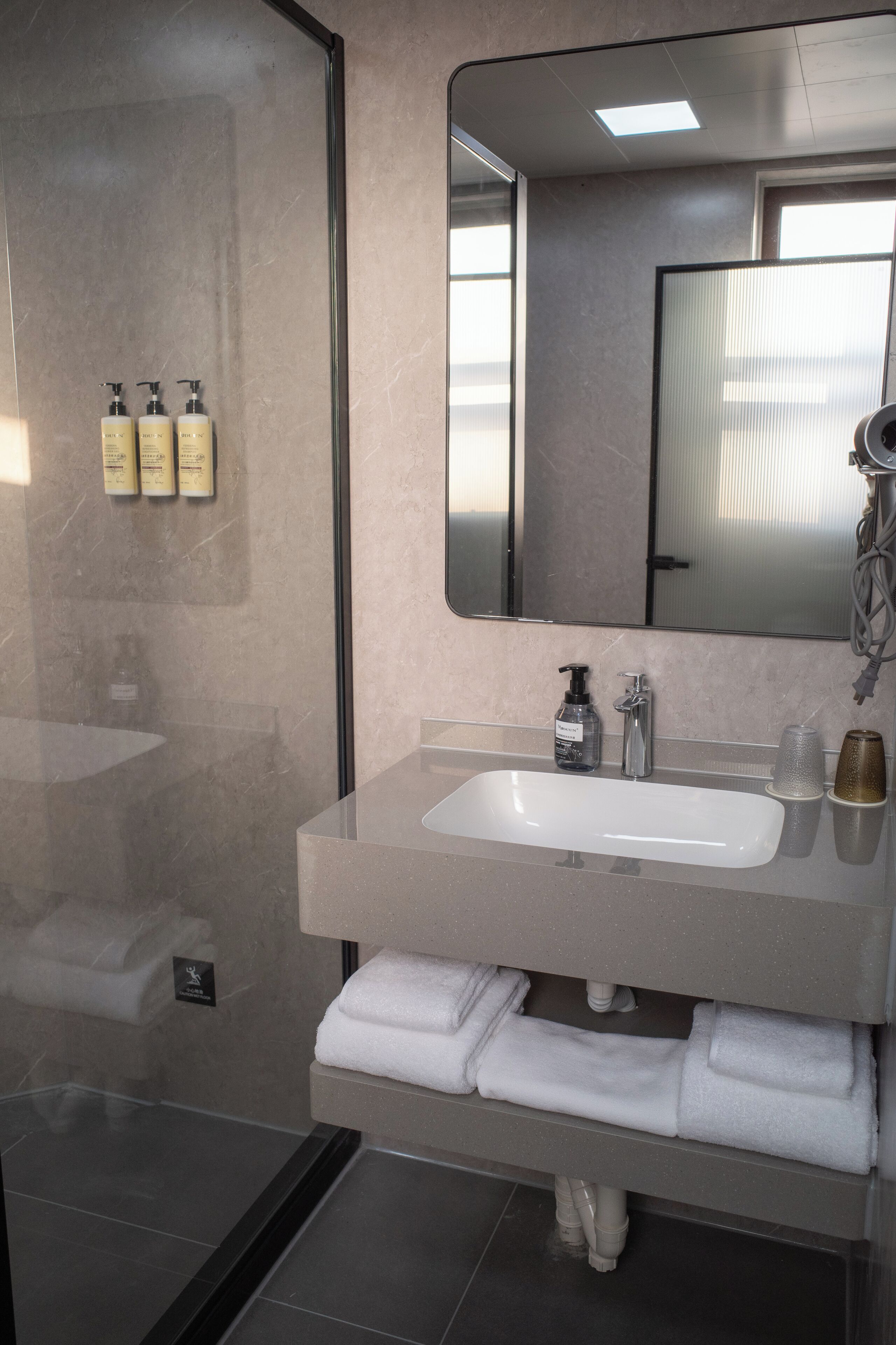A modern bathroom with a glass shower enclosure, a large mirror, and a countertop with toiletries.