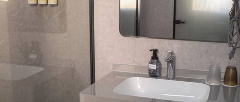A modern bathroom with a glass shower enclosure, a large mirror, and a countertop with toiletries.
