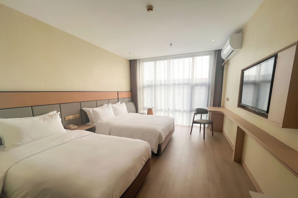 Habitación de hotel con dos camas, un escritorio, una silla, televisión y un amplio ventanal con cortinas.