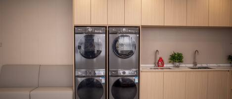 A modern kitchen with two built-in front-loading washing machines, a wooden countertop, a sink, and a small plant.