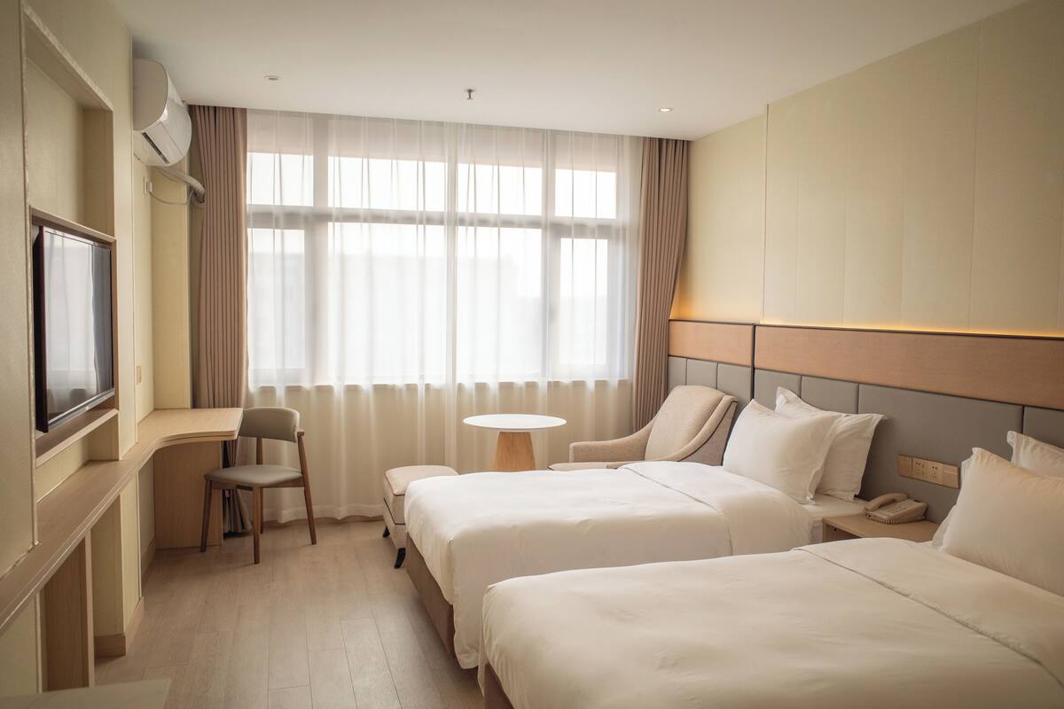 Habitación de hotel con dos camas, un escritorio, una silla, un televisor y una ventana con cortinas.