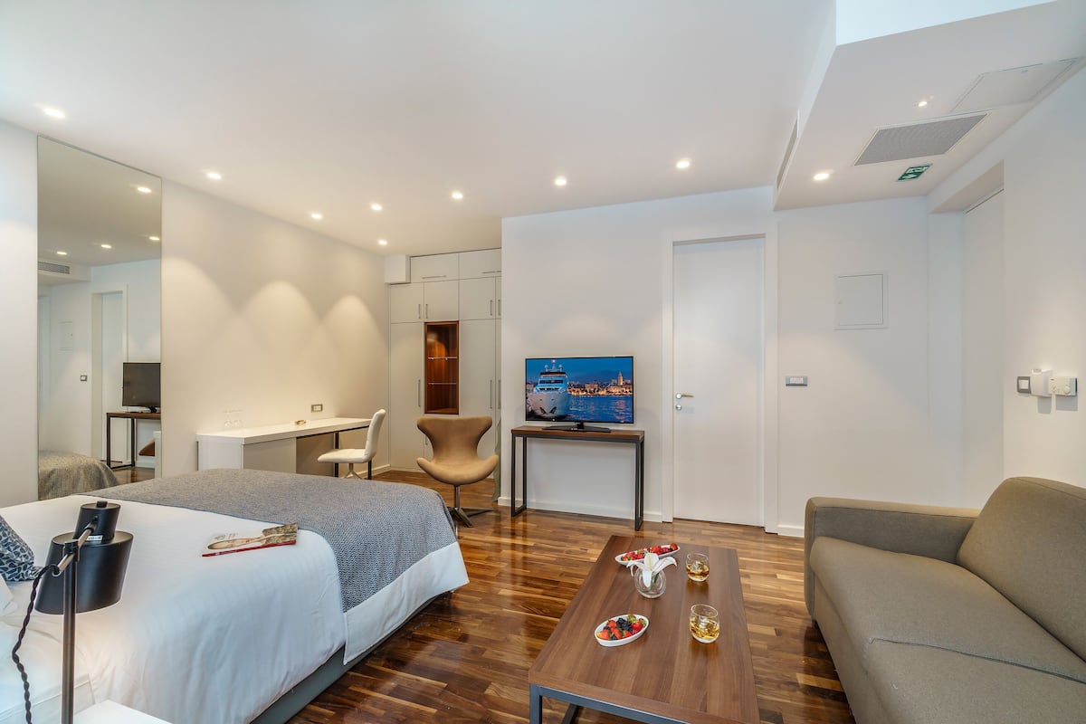 A modern hotel room with a bed, a desk, a sofa, and a dining table with a meal set.