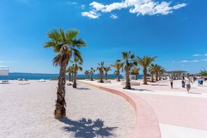 A beach promenade with palm trees, a sandy path, and a clear blue sky.