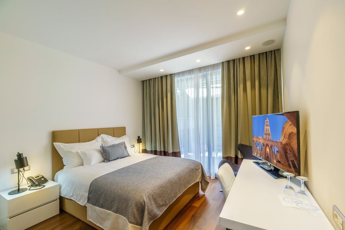 A hotel room with a bed, bedside table, lamp, and a TV displaying a building.