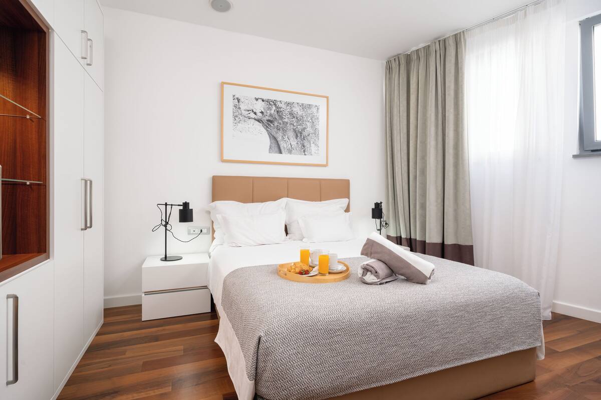 A neatly arranged bedroom with a bed, bedside tables, a framed picture, and a tray with breakfast items.