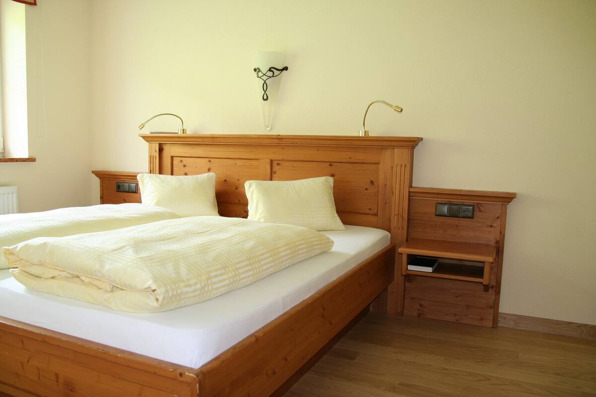 A wooden bed with two pillows and a bedside table with a lamp.