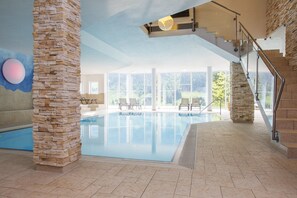 An indoor swimming pool with stone pillars, a staircase, and a view of the outdoors. - Familotel Alphotel (Mittelberg)