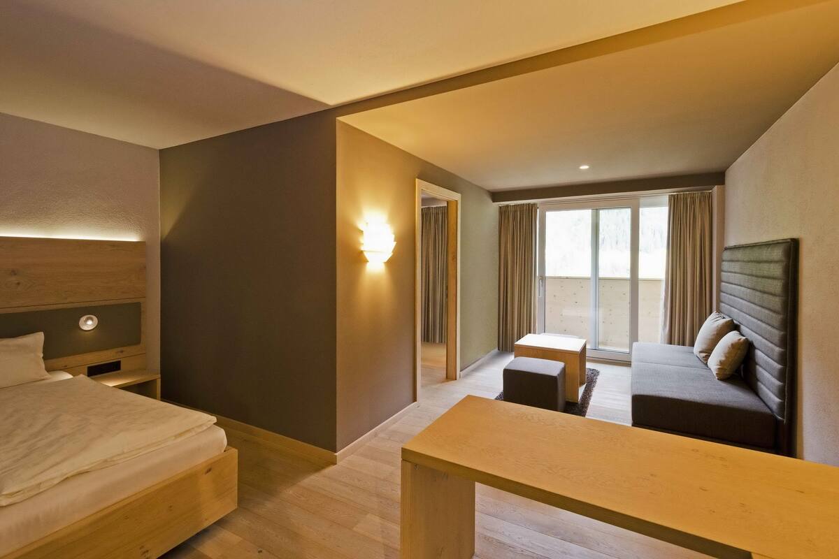 A hotel room with a bed, a desk, a sofa, and a large window.