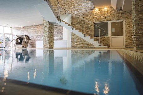 An indoor swimming pool with a wooden house decoration, stone walls, and a staircase.