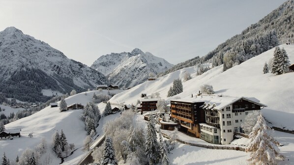 A snow-covered mountain resort with chalet-style buildings, a ski slope, and dense forest. - Familotel Alphotel (Mittelberg)
