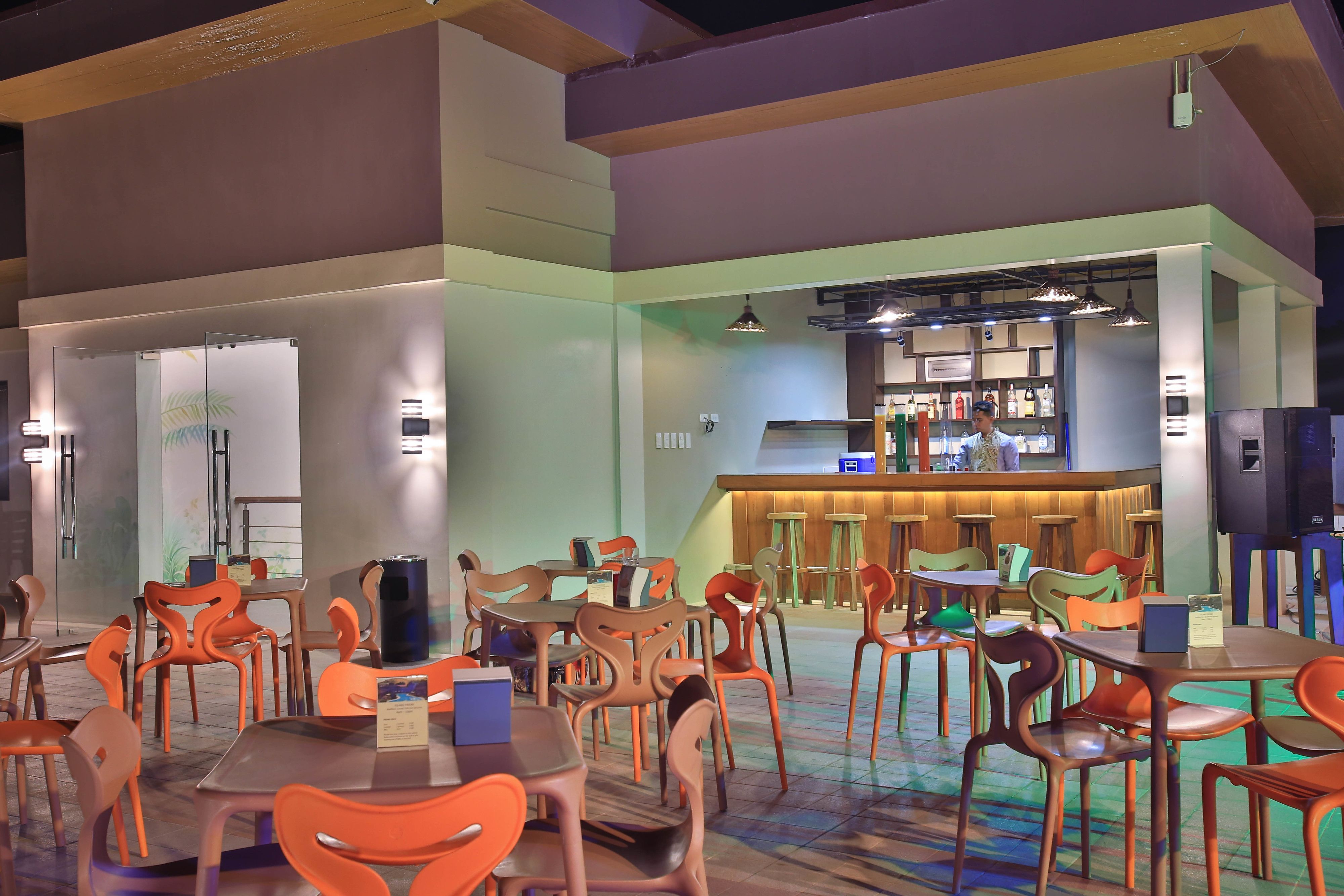 A restaurant with multiple tables and chairs, a bar area, and a counter with a menu.