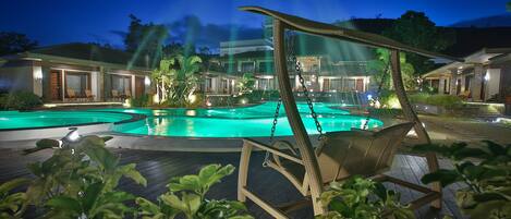 A pool area with a swing chair, a well-lit building, and a clear night sky.