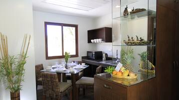 A modern kitchen with a dining area, featuring a glass-top table, wooden chairs, a microwave, and a fruit basket.