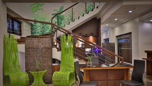 Un moderno vestíbulo de hotel con una escalera, sillas verdes, una recepción y un ventanal grande.