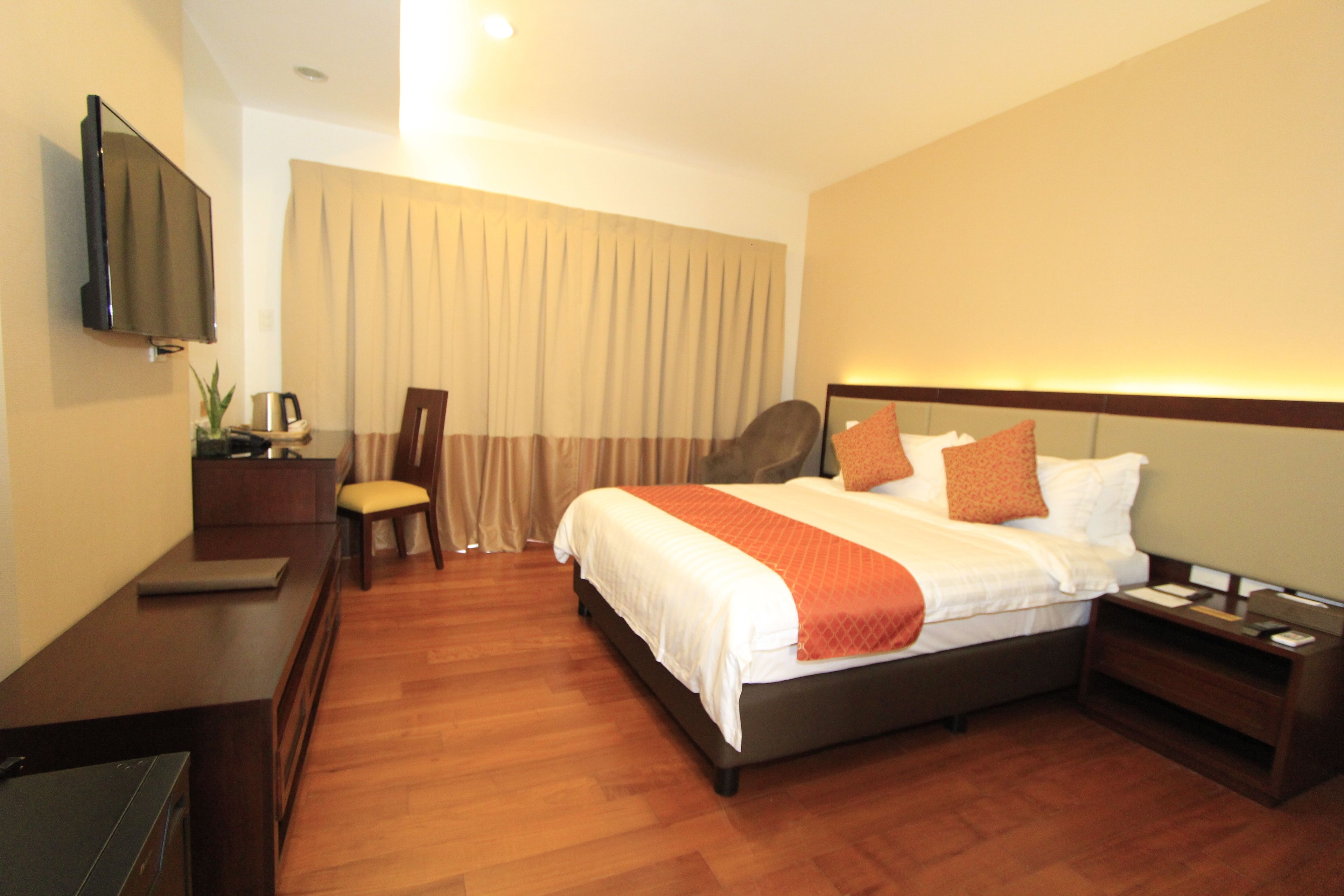 A hotel room with a bed, bedside table, nightstand, TV, and a desk with a chair.