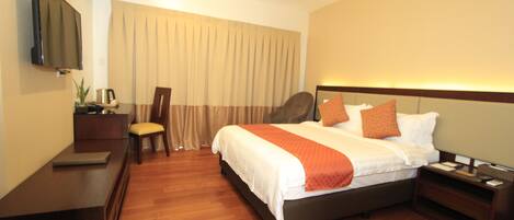 A hotel room with a bed, bedside table, nightstand, TV, and a desk with a chair.