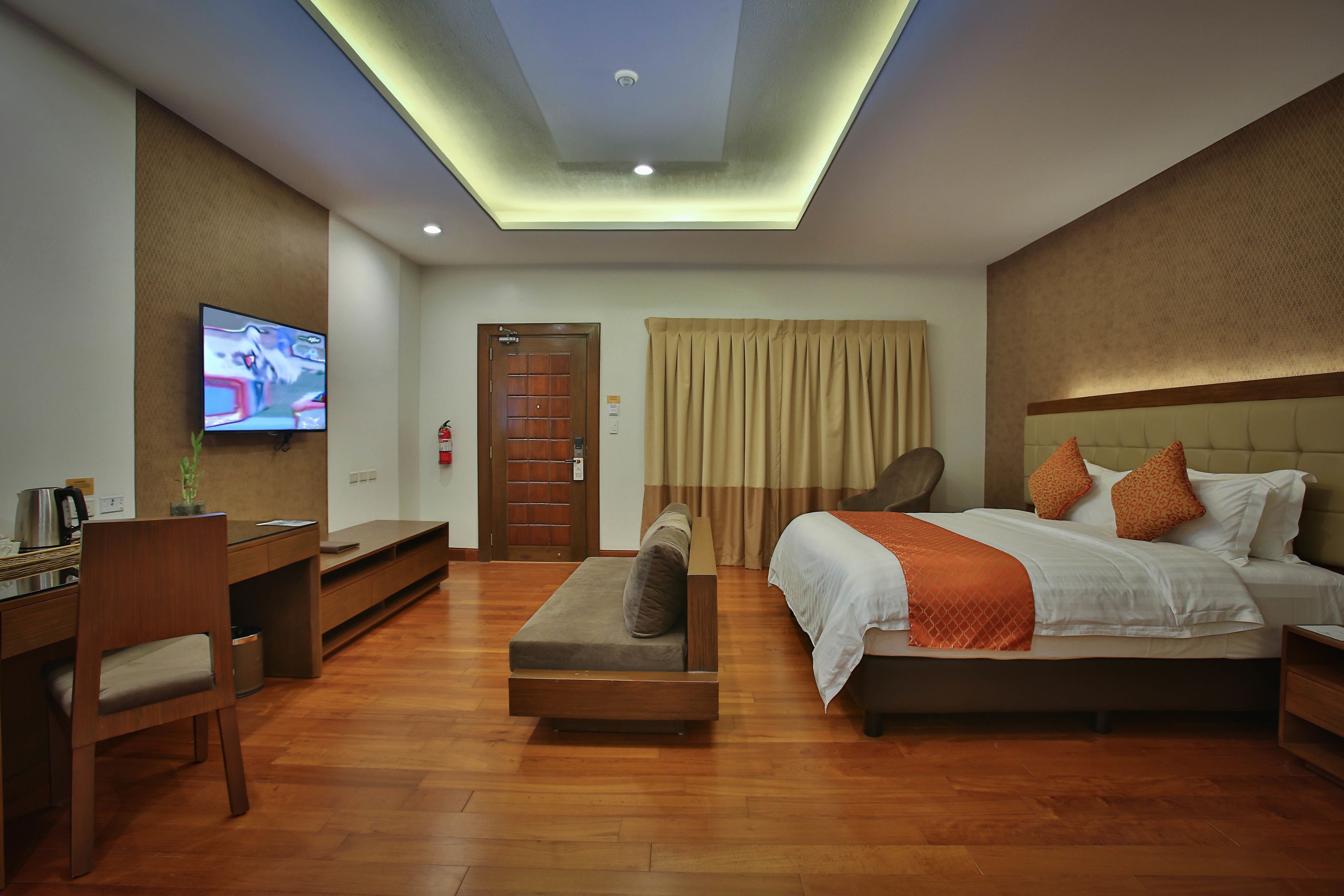 Una habitación de hotel moderna con televisión de pantalla plana, un sofá, una cama con almohadas anaranjadas y suelo de madera.