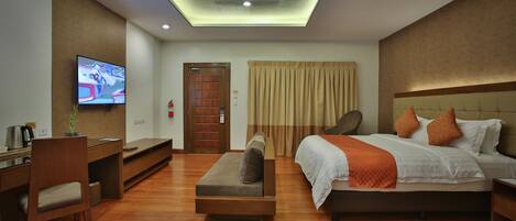 Una habitación de hotel moderna con televisión de pantalla plana, un sofá, una cama con almohadas anaranjadas y suelo de madera.