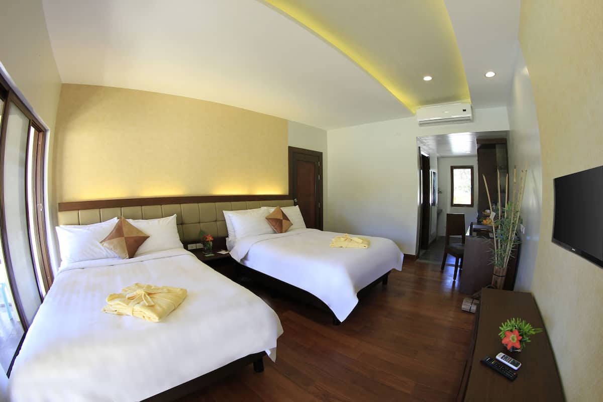 Habitación de hotel con dos camas, suelo de madera, televisor sobre un mueble bajo y una pequeña mesa con el control remoto.