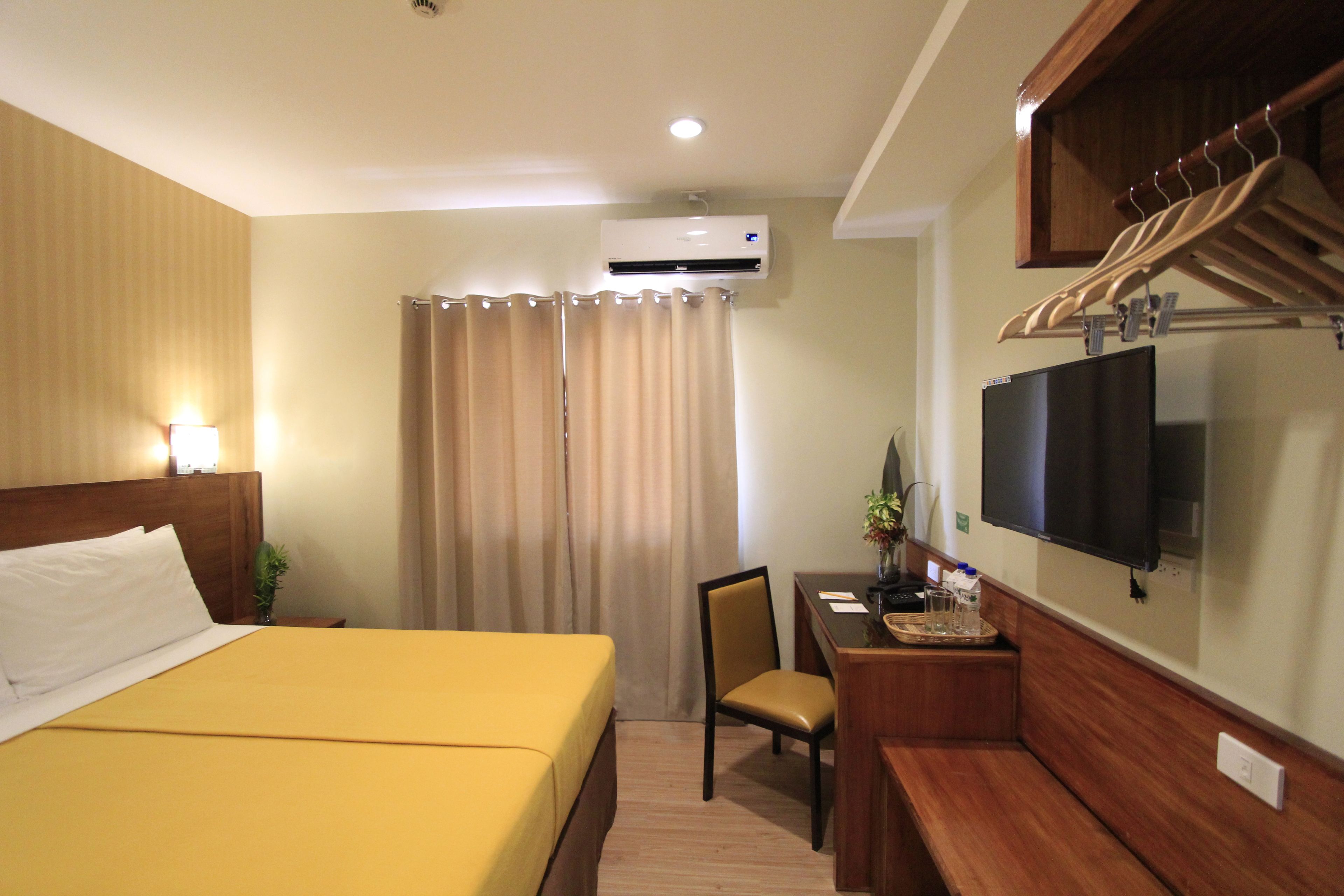 A hotel room with a bed, a desk with a chair, a TV, and a shower area with curtains.